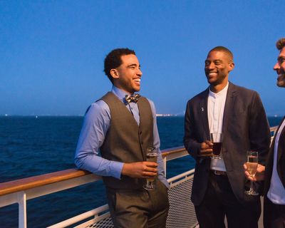 Three men hold drinks on the deck of boat