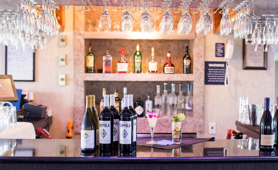 Bottles of wine on top of bar with two mixed drinks