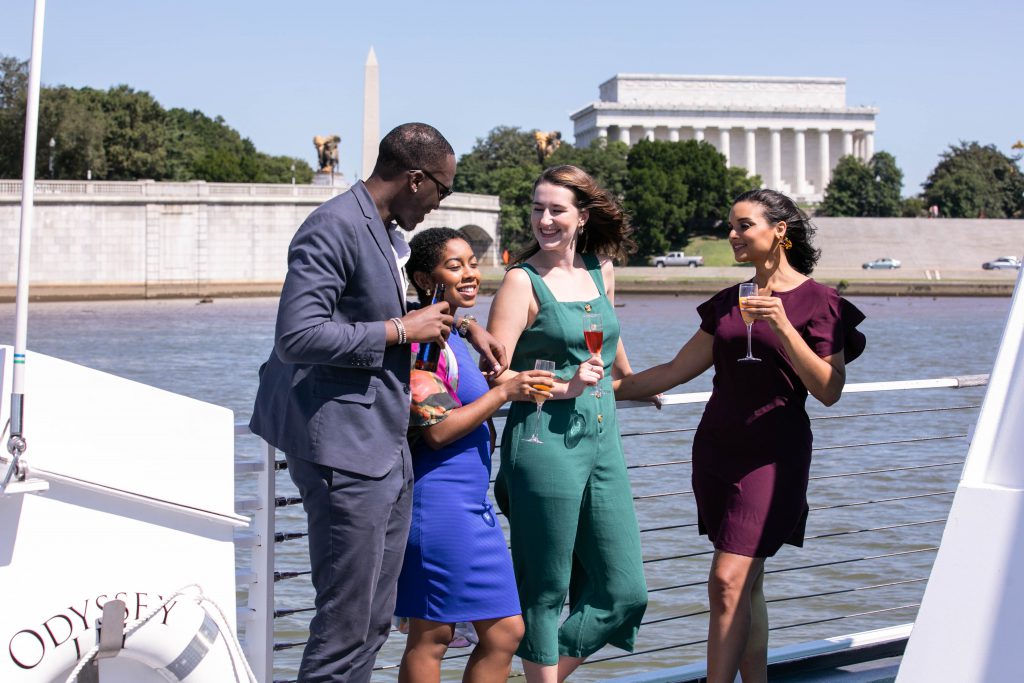 Gente en la cubierta de un barco bebiendo con Washington DC de fondo