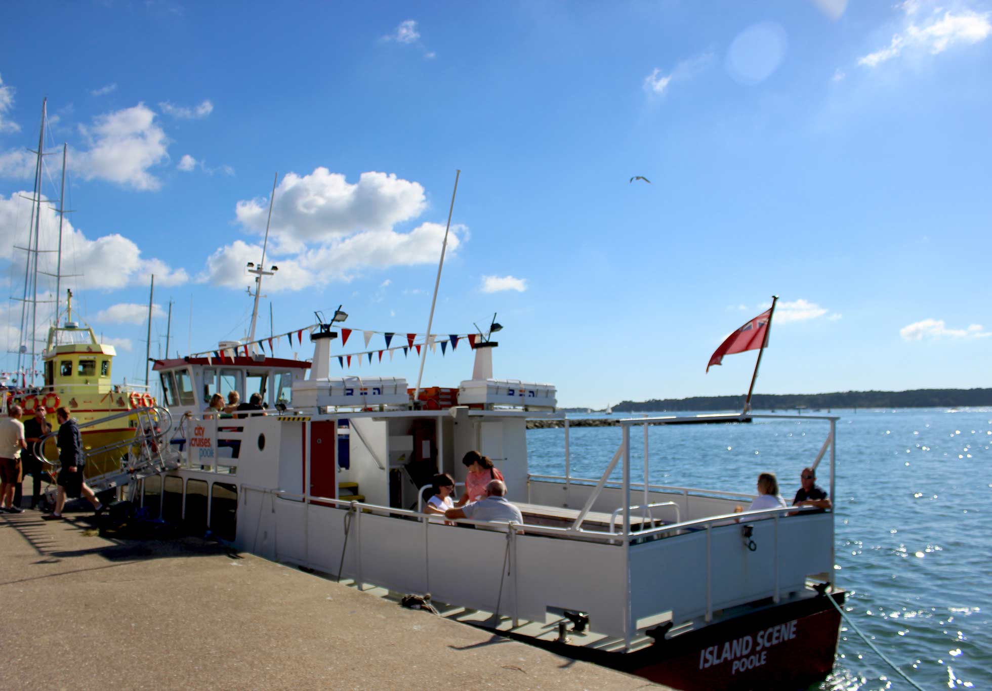 مشهد الجزيرة قارب صغير يرسو في بول مع أشخاص يجلسون على سطح السفينة.
