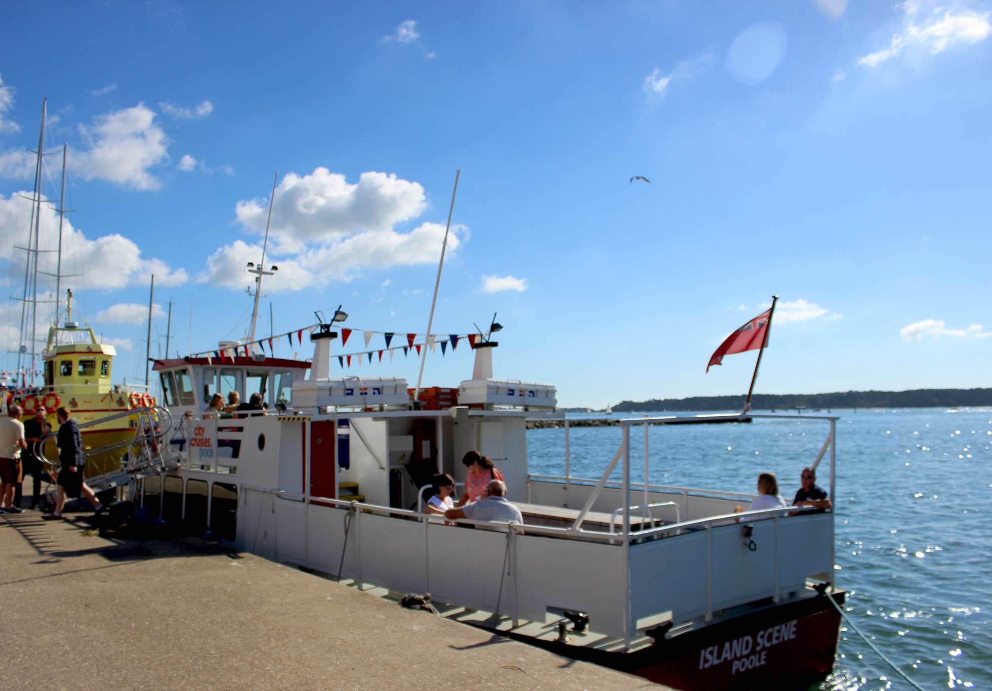 Island Scene ein kleines Boot, das in Poole angedockt ist und auf dessen Deck Menschen sitzen.