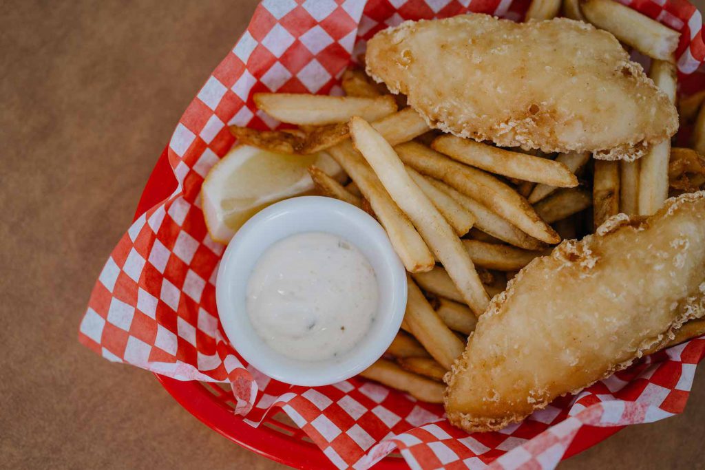 Fish and chips in a basket with red and white checkered paper.