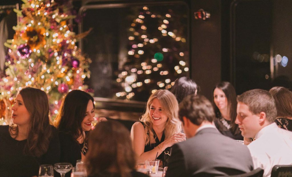 Gruppo di persone sedute a tavola con albero di Natale sullo sfondo.