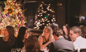 A group of people sitting at table with Christmas tree in background.