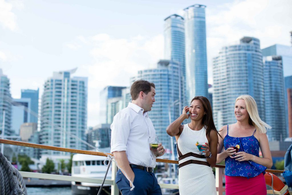 Three people holding drinks with the Toronto skyline in background.