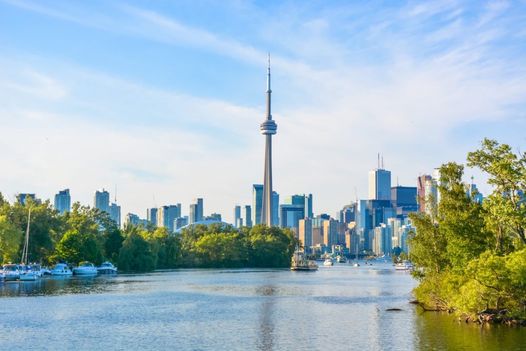 Toronto skyline with boats and trees foreground.