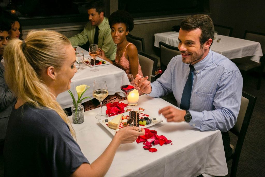 Couple eating dessert with rose petals on table.