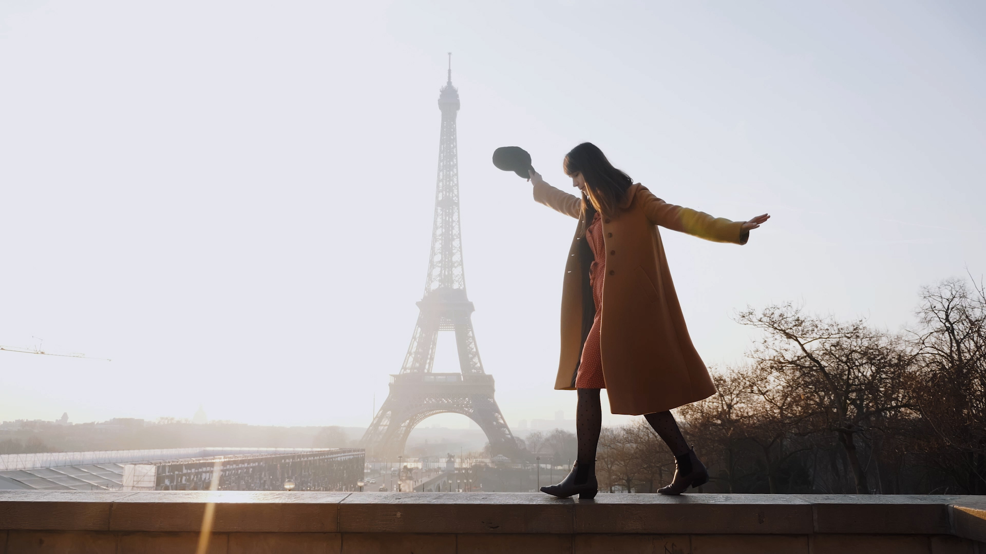 Woman walking on wall ledge with Eiffel Tower in background.