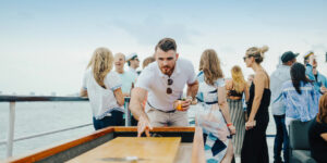 Man playing tabletop shuffle board with group of people behind him.