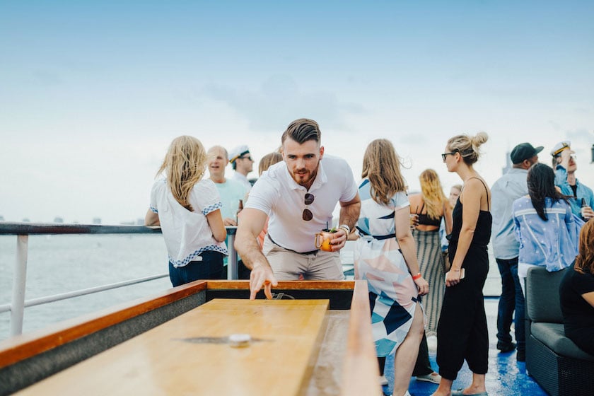 Man playing tabletop shuffle board with group of people behind him.