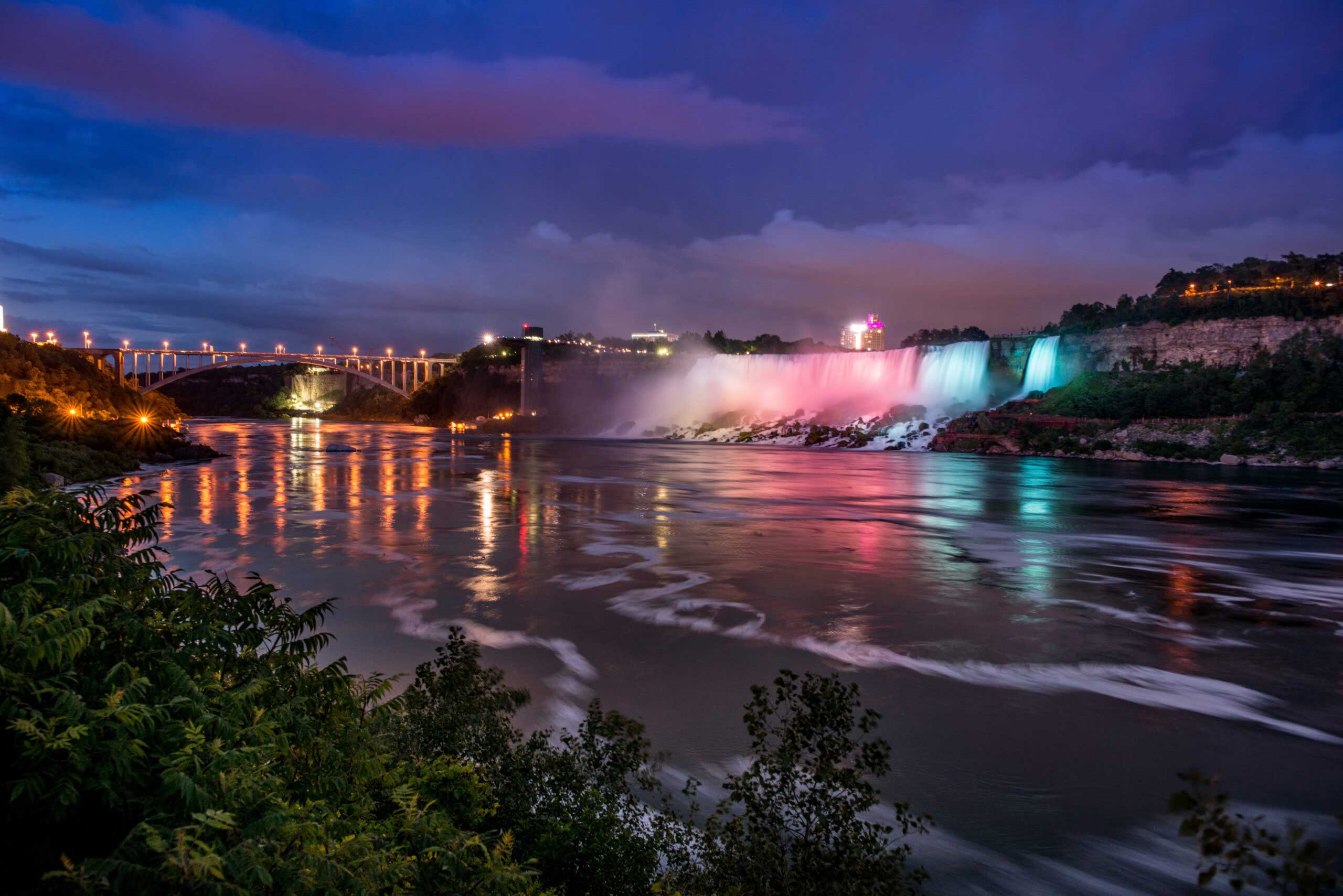 Niagara Falls bij nacht met gekleurde lichten die op de watervallen schijnen.