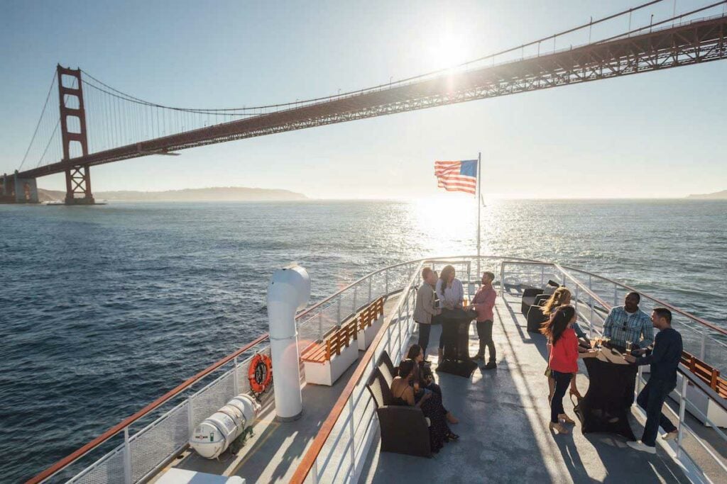 Pessoas na proa do barco com a Ponte Golden Gate em fundo