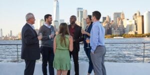 Group of people standing on boat deck with New York City skyline in background.