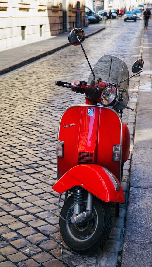 Vespa Vermelha estacionada em pedra de calçada uma rua