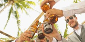 Mænd jubler over ølflasker med palmetræer over dem