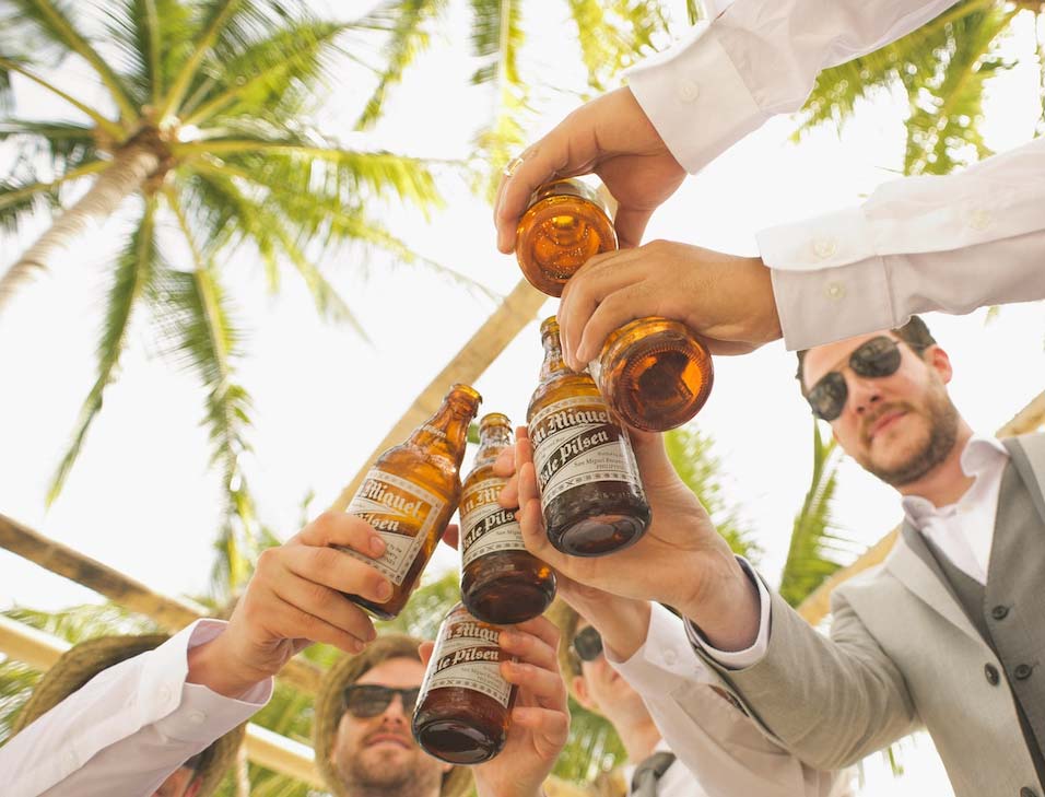 Mannen juichen flessen bier toe met palmbomen erboven