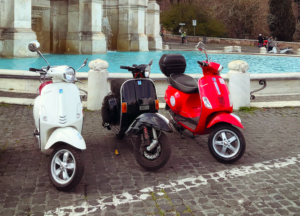 Three Vespa scooters lined up in front of a fountain in Rome Italy