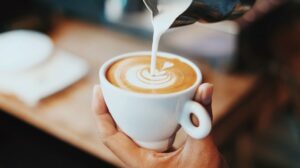 एक डिजाइन बनाने के लिए कॉफी के ऊपर दूध डाला जा रहा है।