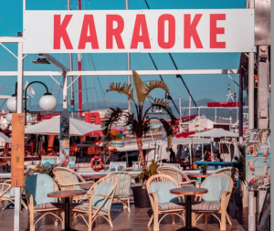 Karaoke-Schild über Tischen draußen an einem Jachthafen
