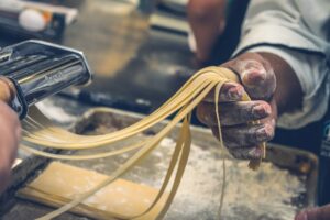 पास्ता बनाने वाले के माध्यम से हाथ से बनाया जा रहा पास्ता