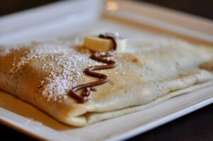Crepes with a banana slice powdered sugar and drizzle of chocolate