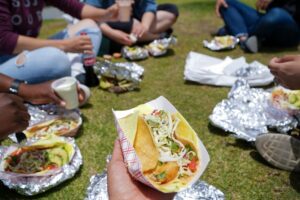 Pessoas a comer tacos sentadas na relva num parque