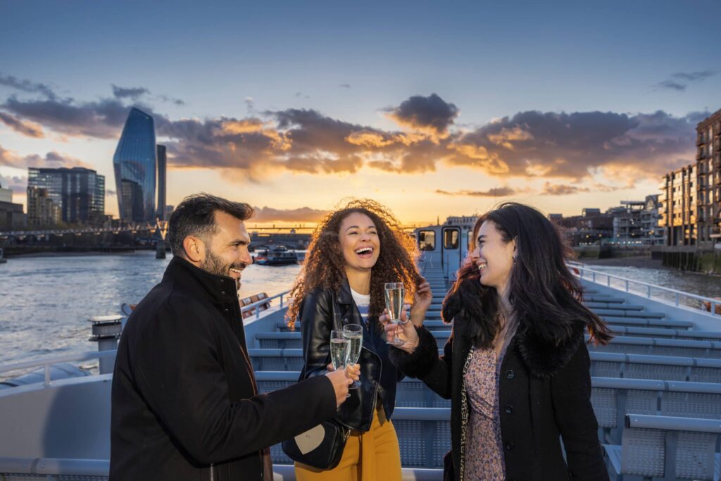 Image of three people cheering champagne on The River Thames in London, UK.