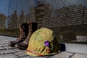Military boots and helmet pinned with a purple heart at base of Vietnam War Memorial