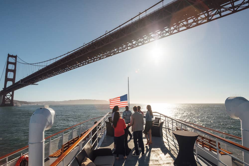 Folk på en båd, der sejler under Golden Gate Bridge
