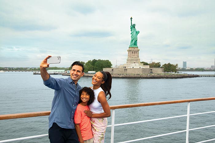 family taking selfie cruising by the statue of liberty